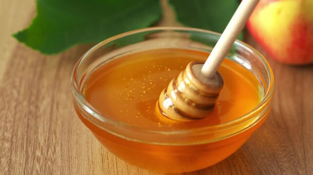 A wooden spoon spindle gathers honey. Golden liquid honey of a fresh harvest is coarse. Apple and honey saved. Beekeeper's Day. Natural bee honey