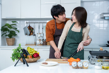 Happy portrait of loving young asian of having fun standing a cheerful preparing food and enjoy cook cooking with vegetables, meat, bread while standing on a kitchen Condo life or home