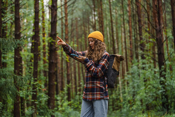 Woman wearing yellow beanie and plaid shirt uses her phone to navigate while pointing in the...