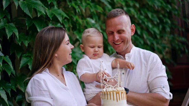 Loving Caucasian parents with their one-year-old baby. Mom and dad hold the cake for their son. First birthday of a child.