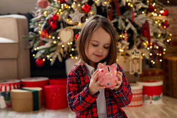 banking, financial, investment and happy people concept - beautiful girl puts coins into pink piggy bank on Christmas. pocket money, family budget and savings concept.