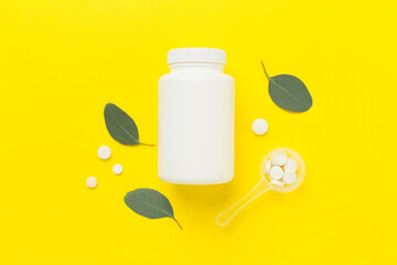 Bottle with pills and green leaves on color background, top view
