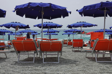 Sunlounger reclining seats and parasol umbrellas are shown at a seaside beach during a summer day.