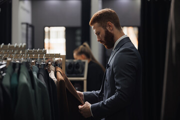 Portrait handsome client man in menswear store chooses suit. Luxury designer atelier shop