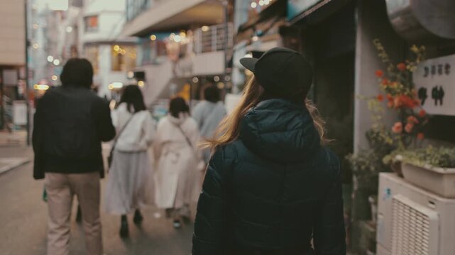 Stylish blonde woman leads her friends through tokyo's bustling streets, exuding a modern vibe in a black cap and jacket