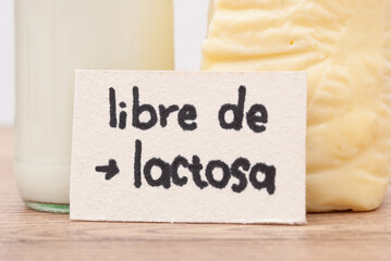 Milk in glassware and a piece of cheese, card with the phrase “Lactose free” on wooden table. Space for text