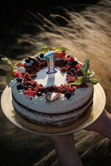 A delicious red velvet cake for a first birthday, decorated with fresh fruit (physalis, blueberries, raspberries, currants, and blackberries). Finished with red velvet crumbs and milk chocolate.