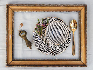 A decorative table setting features a patterned plate and bowl, a gold spoon, and a vintage bottle...