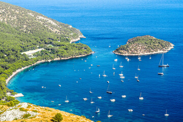 A beautiful view of a tranquil bay on Mallorca, where the vibrant blue waters are dotted with sailboats. Lush green hills embrace the coastline, offering a perfect contrast to the clear Mediterrane.