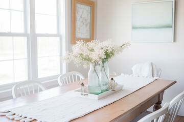 A rustic wooden dining table adorned with a crisp white tablecloth and a centerpiece of white flowers in glass jars. Large windows flood the room with natural light,