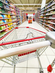 Pusty koszyk, wózek sklepowy w supermarkecie, rozmazane tło, wnętrze sklepu, supermarketu, wózek na zakupy, półki sklepowe z produktami. Hipermarket. Miejsce na tekst.