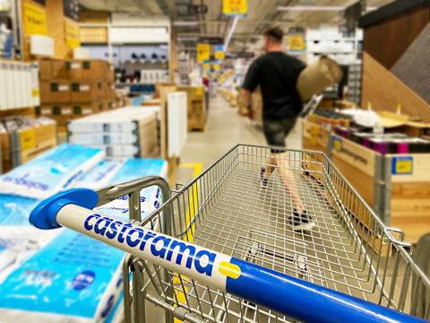 Pusty koszyk, w&oacute;zek sklepowy w supermarkecie, rozmazane tło, wnętrze sklepu, supermarketu, w&oacute;zek na zakupy, p&oacute;łki sklepowe z produktami. Hipermarket Castorama. Warszawa, CH Wola Park. Miejsce na tekst