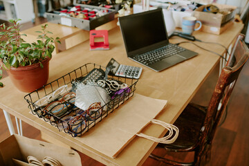 Work desk filled with various office supplies including a laptop, wire basket of glasses, stationery, and a potted plant contributing to an organized workspace