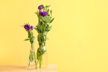 Vase with eustoma flowers on table near yellow wall