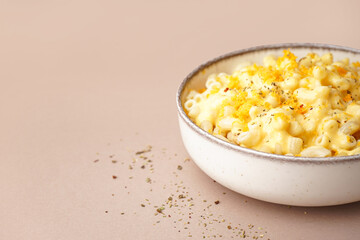 Bowl of tasty Italian pasta with Cheddar cheese on beige background, closeup