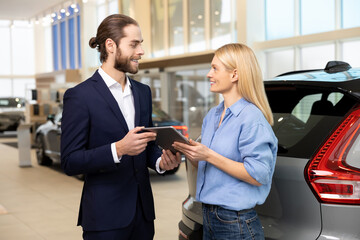 Woman finalizing buying of luxury vehicle with the customer service manager at auto dealership