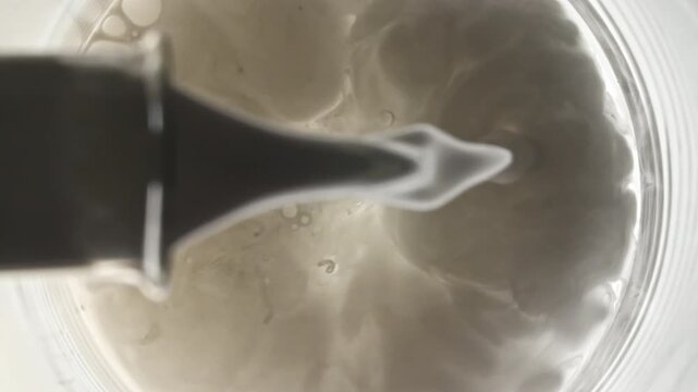 Liquid pouring into beaker with water from glass flask on white background. The medicine concept, health care, treatment. Skin care product. Macro Shot. High quality 4k footage