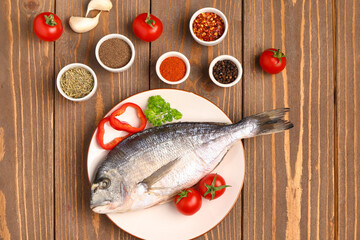 Plate of raw dorado fish with tomatoes and spices on wooden background