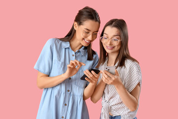 Young women in eyeglasses using mobile phones on pink background