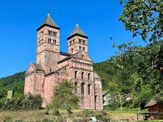 View of the historic Abbaye de Murbach with its Romanesque architecture, surrounded by lush greenery under a clear blue sky near Guebwiller in Florival, Haut-Rhin, Alsace, France