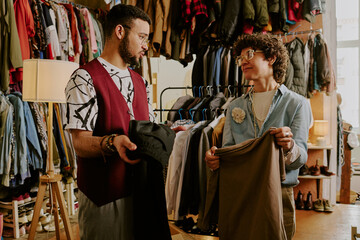 Two people discussing fashion choices inside a clothing boutique, surrounded by various garments on...