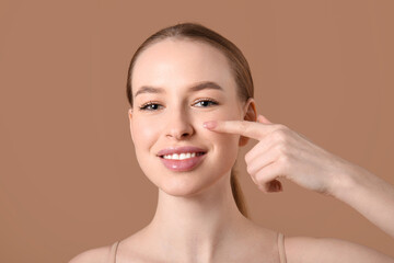 Beautiful young woman pointing at face on brown background