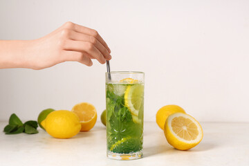 Female hand with glass of lemonade, lemons and straw on white background