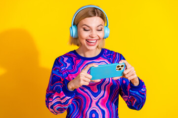 Photo portrait of lovely young lady headphones play mobile game dressed stylish colorful blue garment isolated on yellow color background