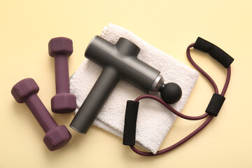 Percussive massager, clean towel, expander and dumbbells on color background