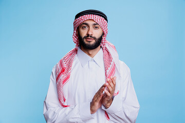 Muslim man in thobe and ghutra applauding with hands, showing support and approval studio portrait....
