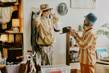 A person trying on a hat while interacting with another person in cozy vintage clothing store...