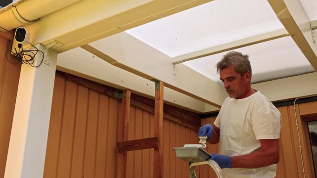 Close-up of a man using a roller to paint a patio frame white at his house. Sweden.