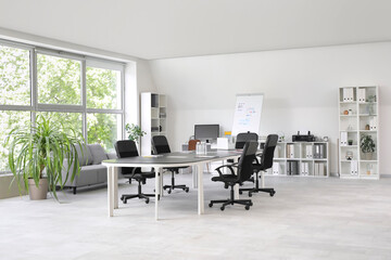 Interior of light conference hall with big table, armchairs, shelving unit and houseplant