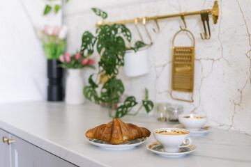 A cozy breakfast setting with a croissant and coffee next to a plant and floral arrangement