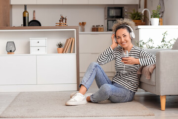 Beautiful middle-aged woman with glass of wine and headphones listening to music at home