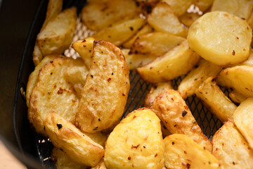 Golden crispy roasted potato wedges close-up. A close-up of golden, crispy roasted potato wedges, seasoned with herbs and spices, served on a white plate.

