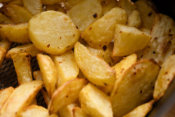 Golden crispy roasted potato wedges close-up. A close-up of golden, crispy roasted potato wedges, seasoned with herbs and spices, served on a white plate.

