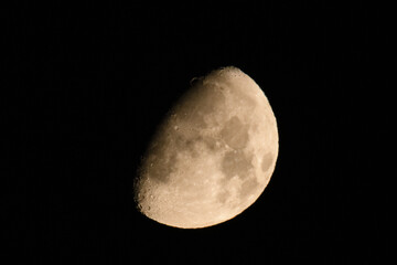 Waxing gibbous moon against dark night sky. Close-up of the waxing gibbous moon glowing against a dark night sky, showing craters and surface details in warm tones.

