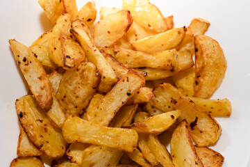 Golden crispy roasted potato wedges close-up. A close-up of golden, crispy roasted potato wedges, seasoned with herbs and spices, served on a white plate.

