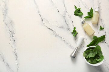 Bottles of essential oil, mortar, pestle and mint leaves on marble background
