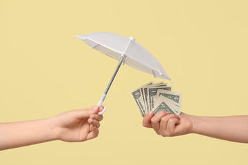 Female hands with mini umbrella and money on yellow background