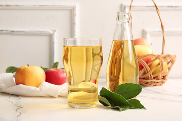 Composition with fruits, wicker basket, bottle and glass of fresh tasty apple cider on table