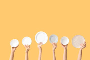 Hands holding empty plates on yellow background