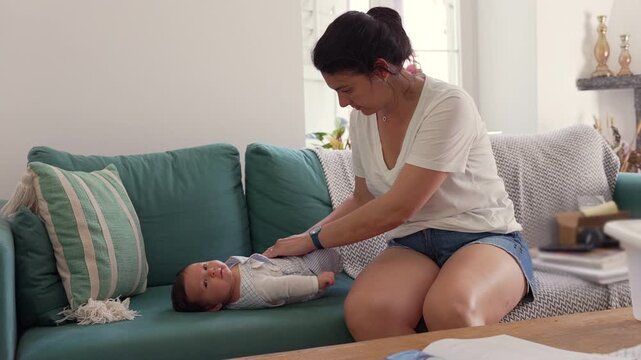 Mother gently massages her baby's tummy while the baby lies on the sofa, helping to relieve gas and provide comfort.  relaxed home setting highlights a nurturing and caring moment