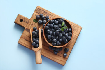 Wooden cutting board, scoop and bowl with fresh ripe blueberry on blue background