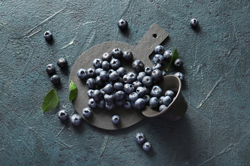 Cutting board and bowl with fresh ripe blueberry on dark blue grunge background