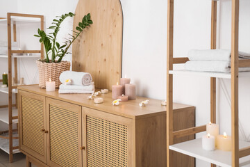 Towels with burning candles and plumeria flowers on commode in spa salon