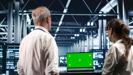 Certified IT programmers looking around high tech data center, using green screen laptop to crosscheck disaster recovery plan and assess server systems in need of replacement, preventing failures