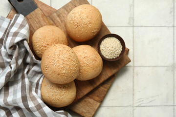 Wooden board of fresh buns with sesame seeds on white tile background