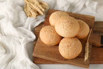 Wooden board of fresh buns with sesame seeds and wheat on white background